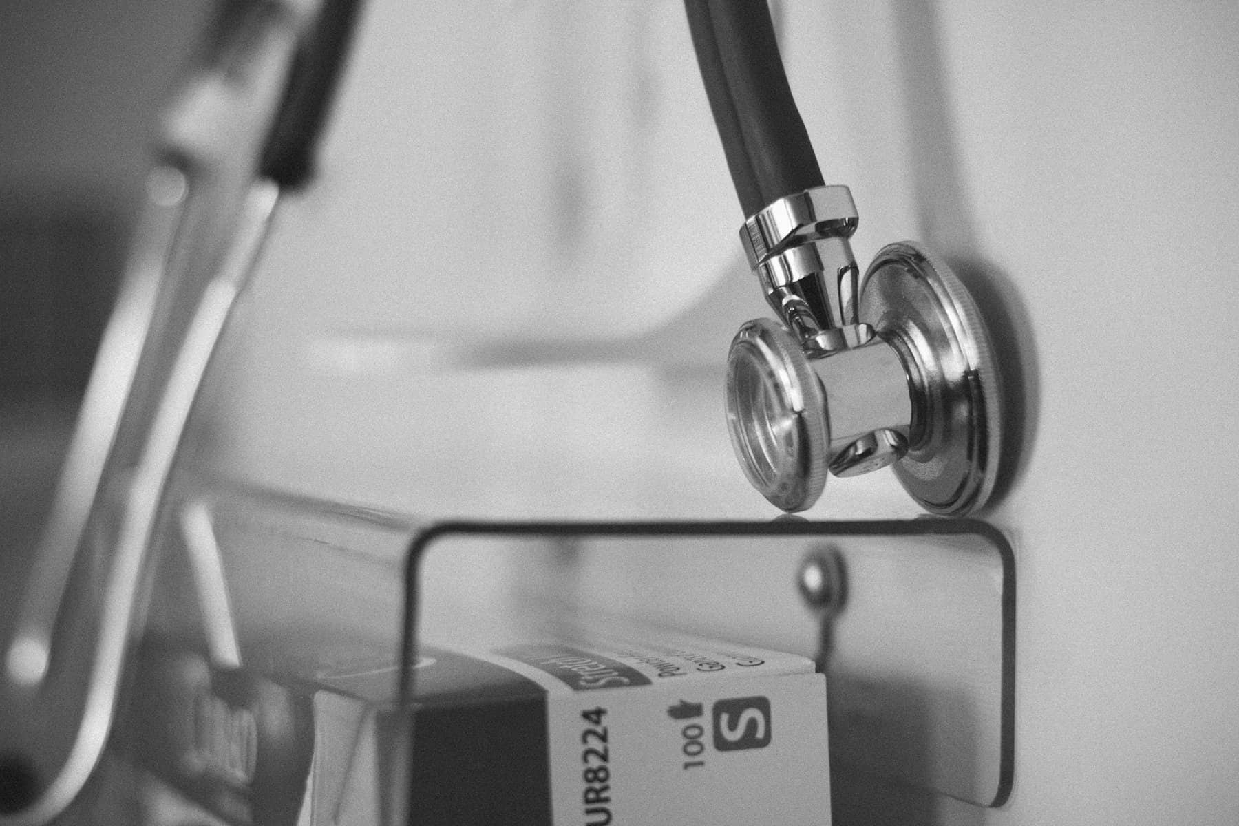 Black and white photo shows a stethoscope hanging near other medical supplies.