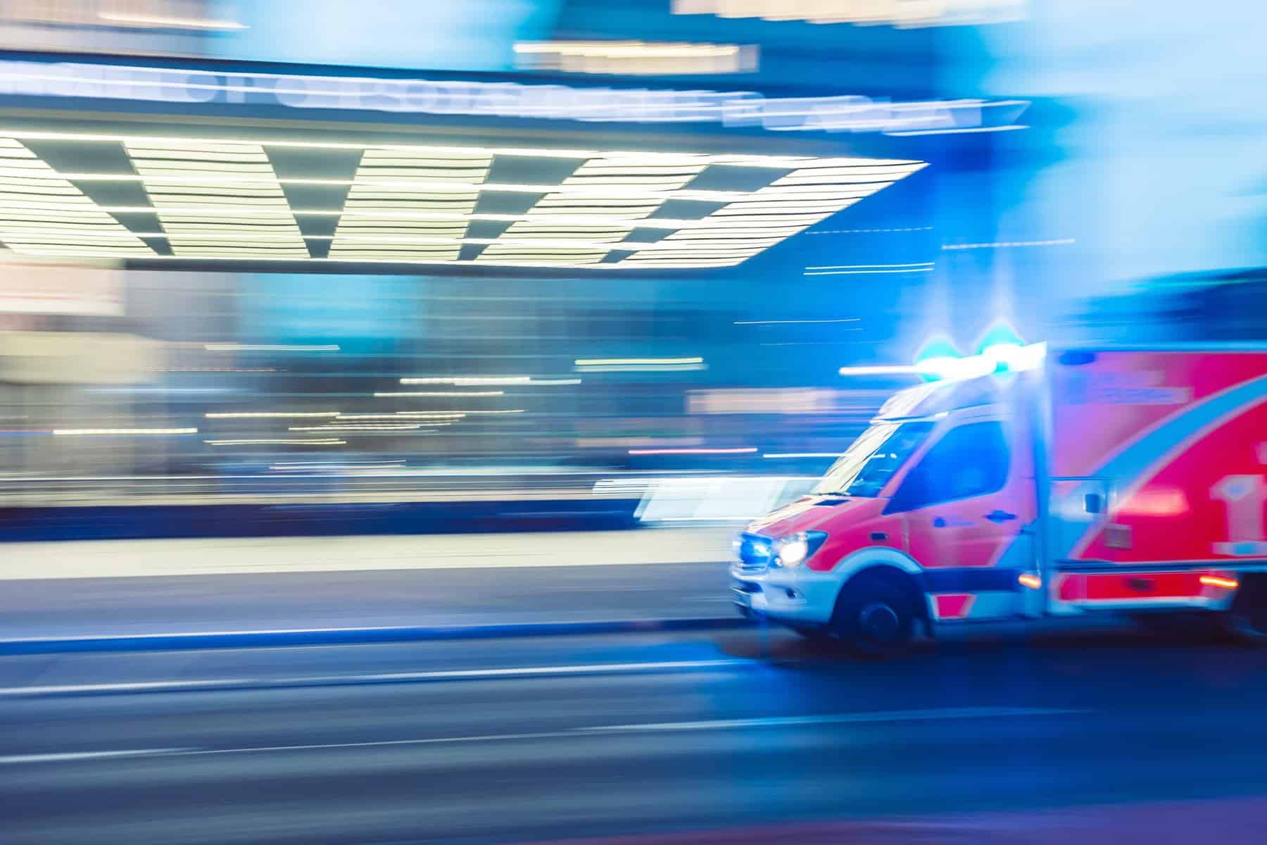 The front end of a red ambulance is seen on image right speeding past a blurred building.