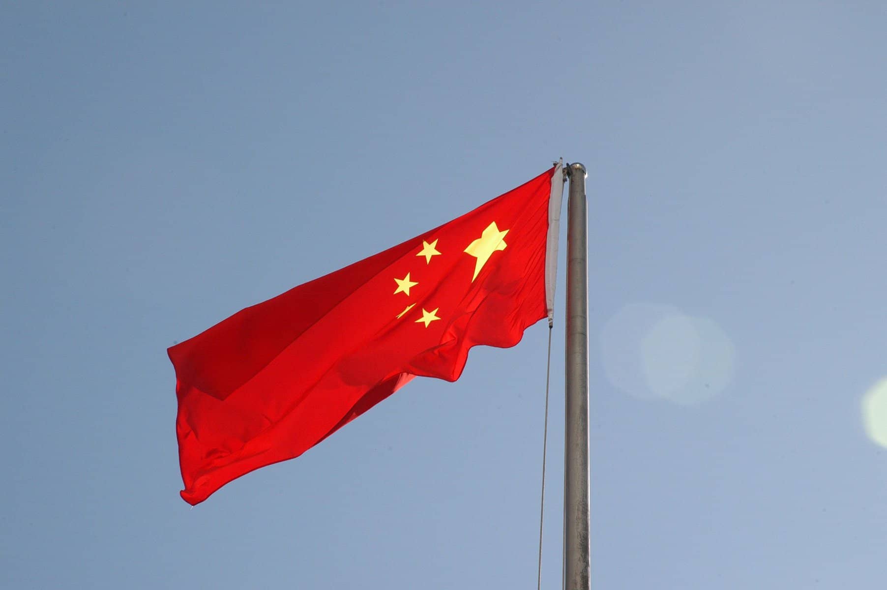 The flag of China waves against a grey sky.