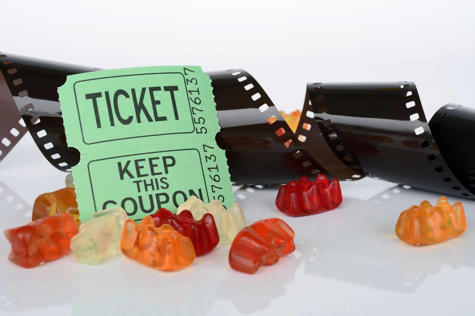 Green ticket stubs are shown on a white surface with a roll of film spiraled behind them and gummy candy in front.