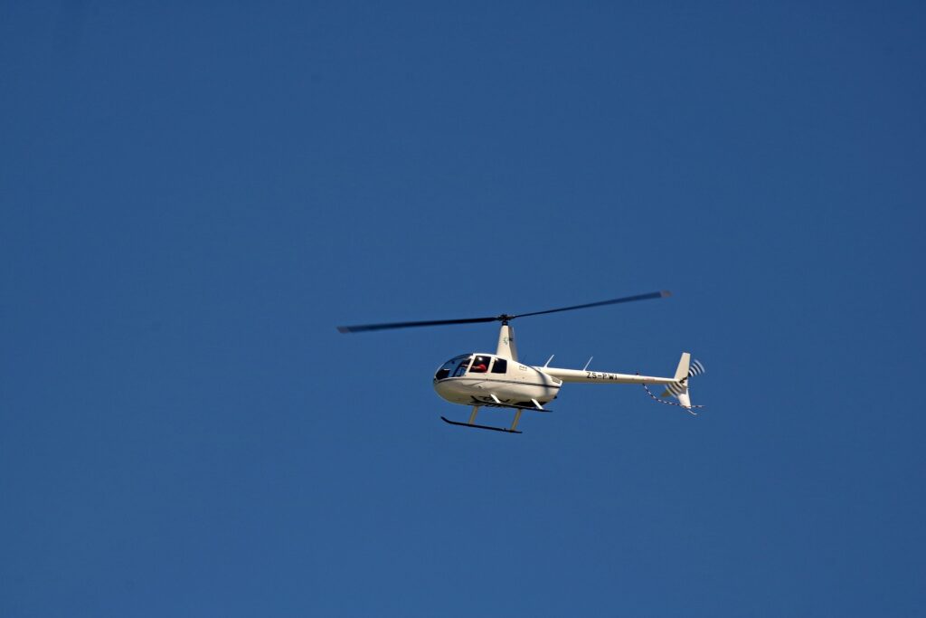 A commercial helicopter is shown high up against a blue sky.