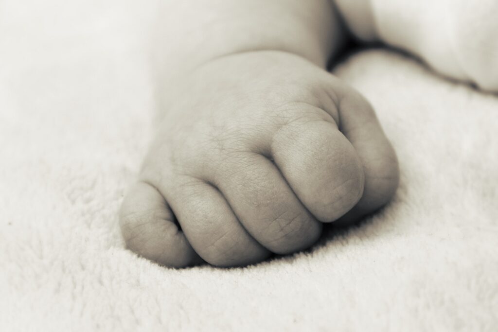 Sepia image shows an infant's hand is shown resting on a soft surface with hand in a soft fist.