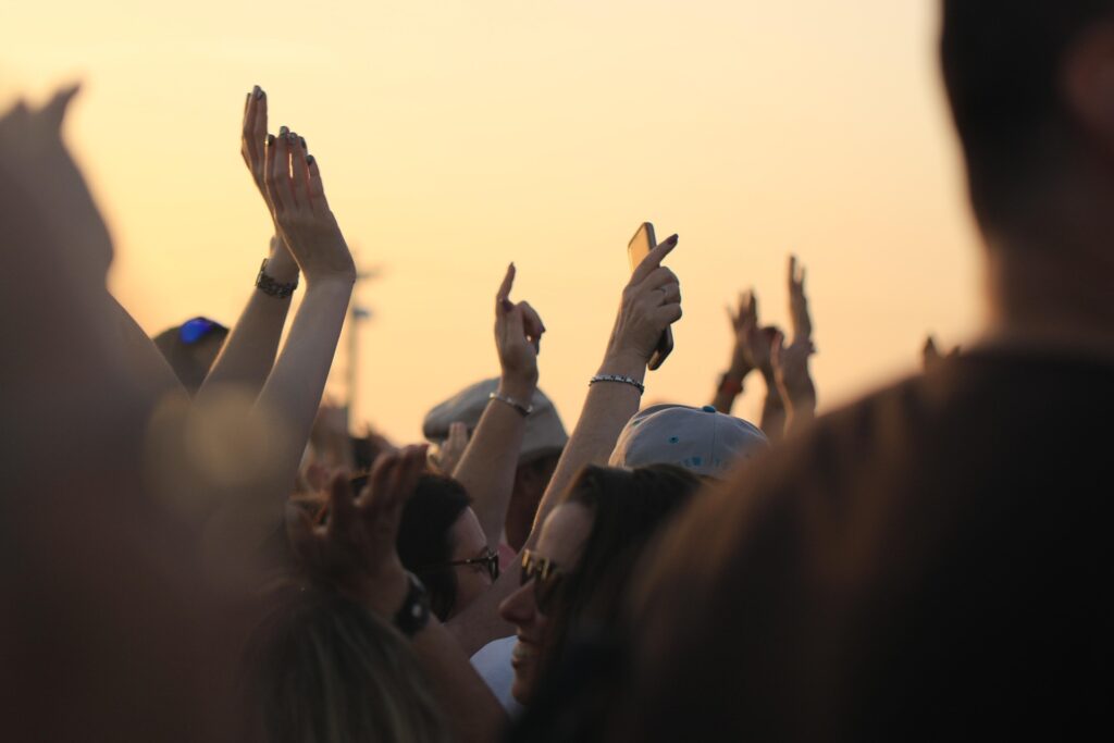 Many hands from a crowd are seen thrust up to the sky at dusk.