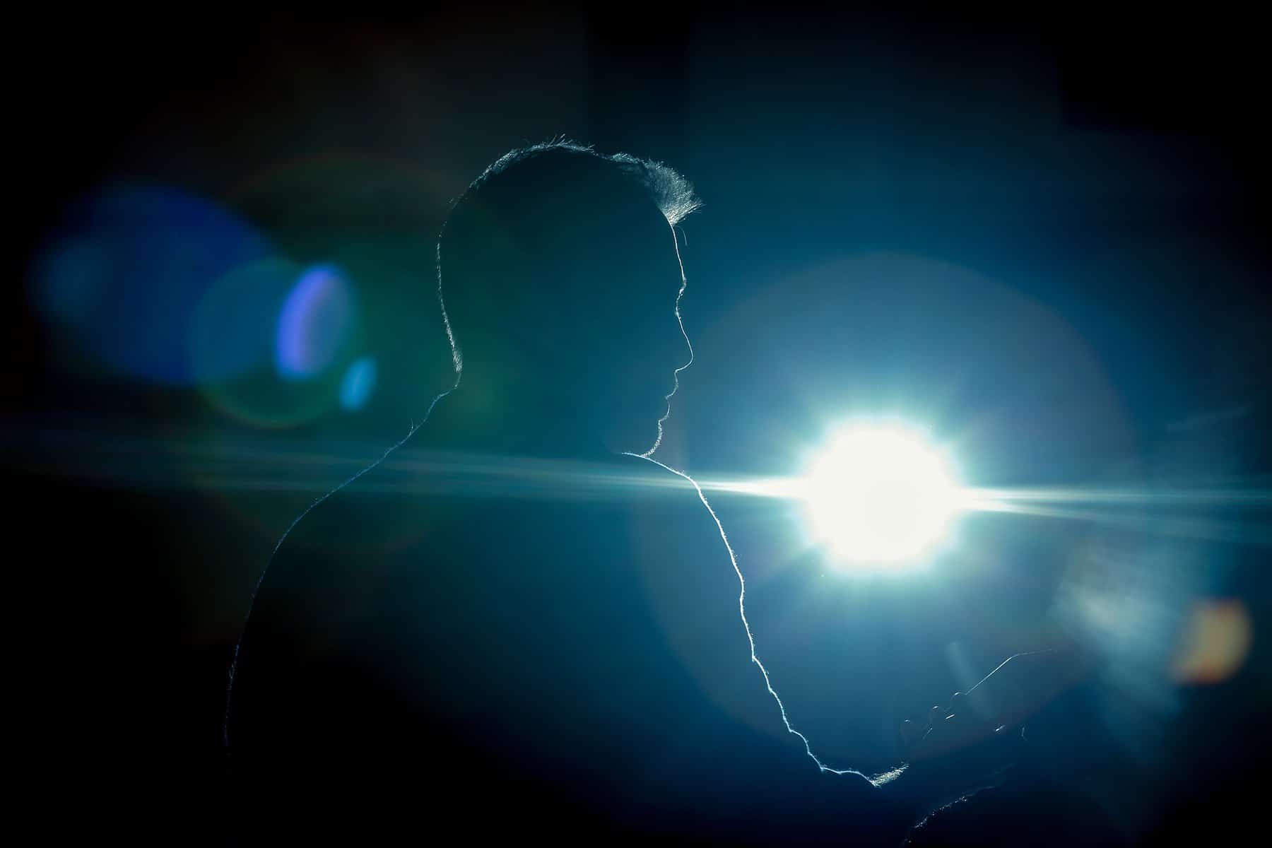 A man is shown in silhouette with stage lighting shining toward the camera.