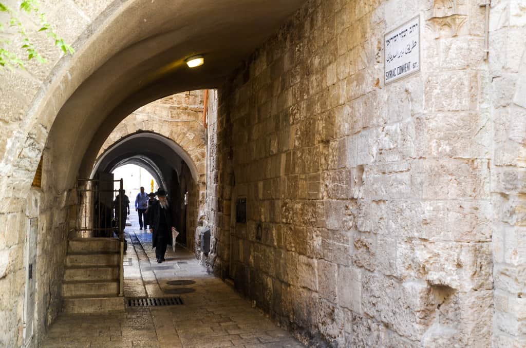 People are seen walking through a tunnel like stone building.