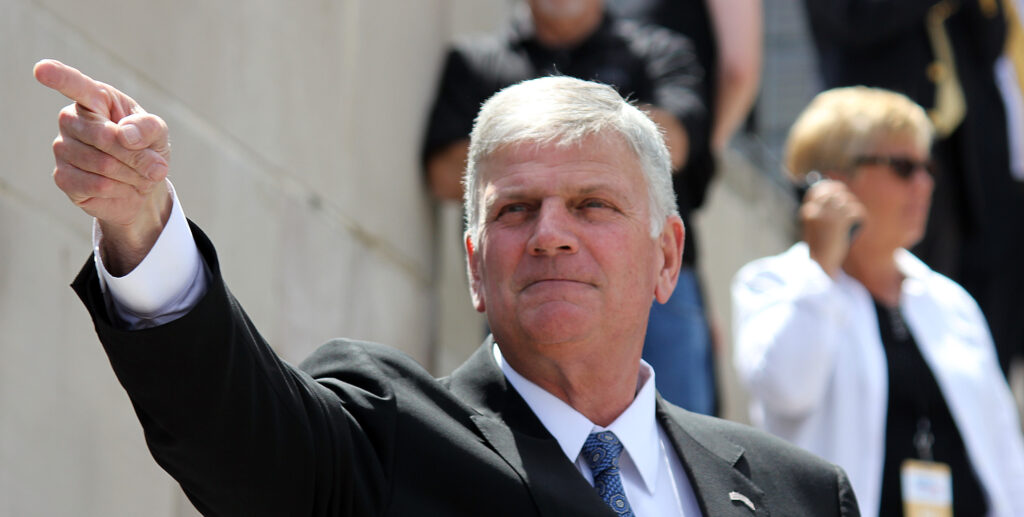 Franklin Graham is shown in a suit with an arm extended to a pointing finger.