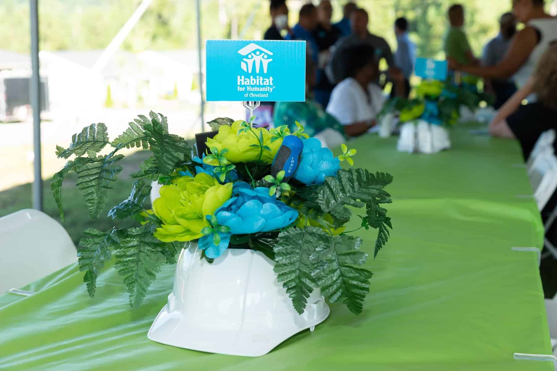 A white hard hat decorated with green and blue silk flowers sits on a table at a Habitat for Humanity affiliate event.