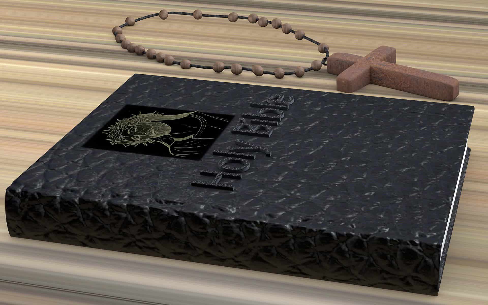 A black bible is shown on a table next to a wooden rosary with a large cross.