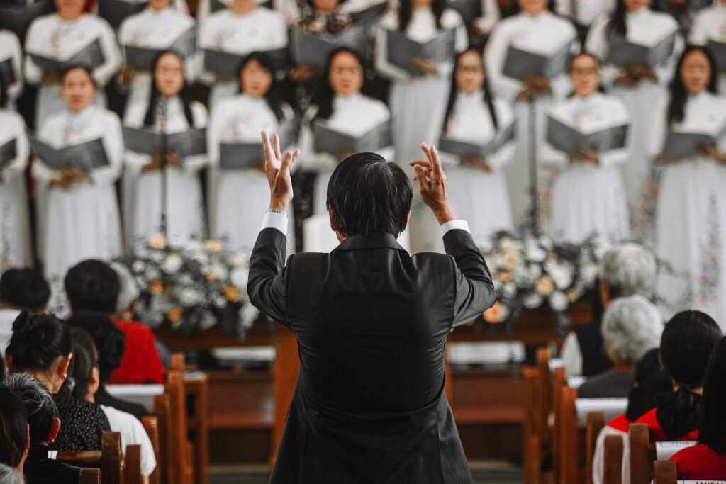 A male choir director is shown from the back directing a choir dressed in robes.