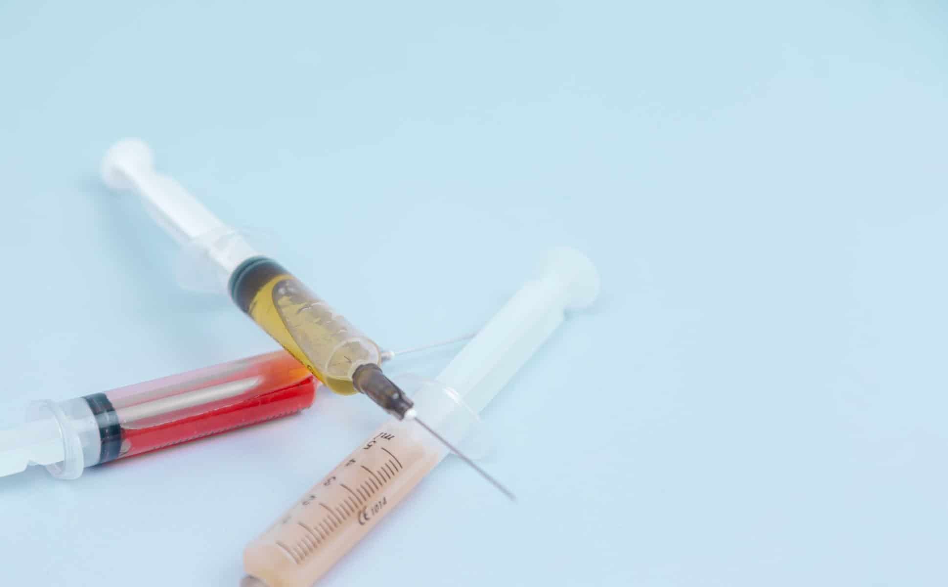 Three hypodermic needles filled with different color liquids lay on a white surface.