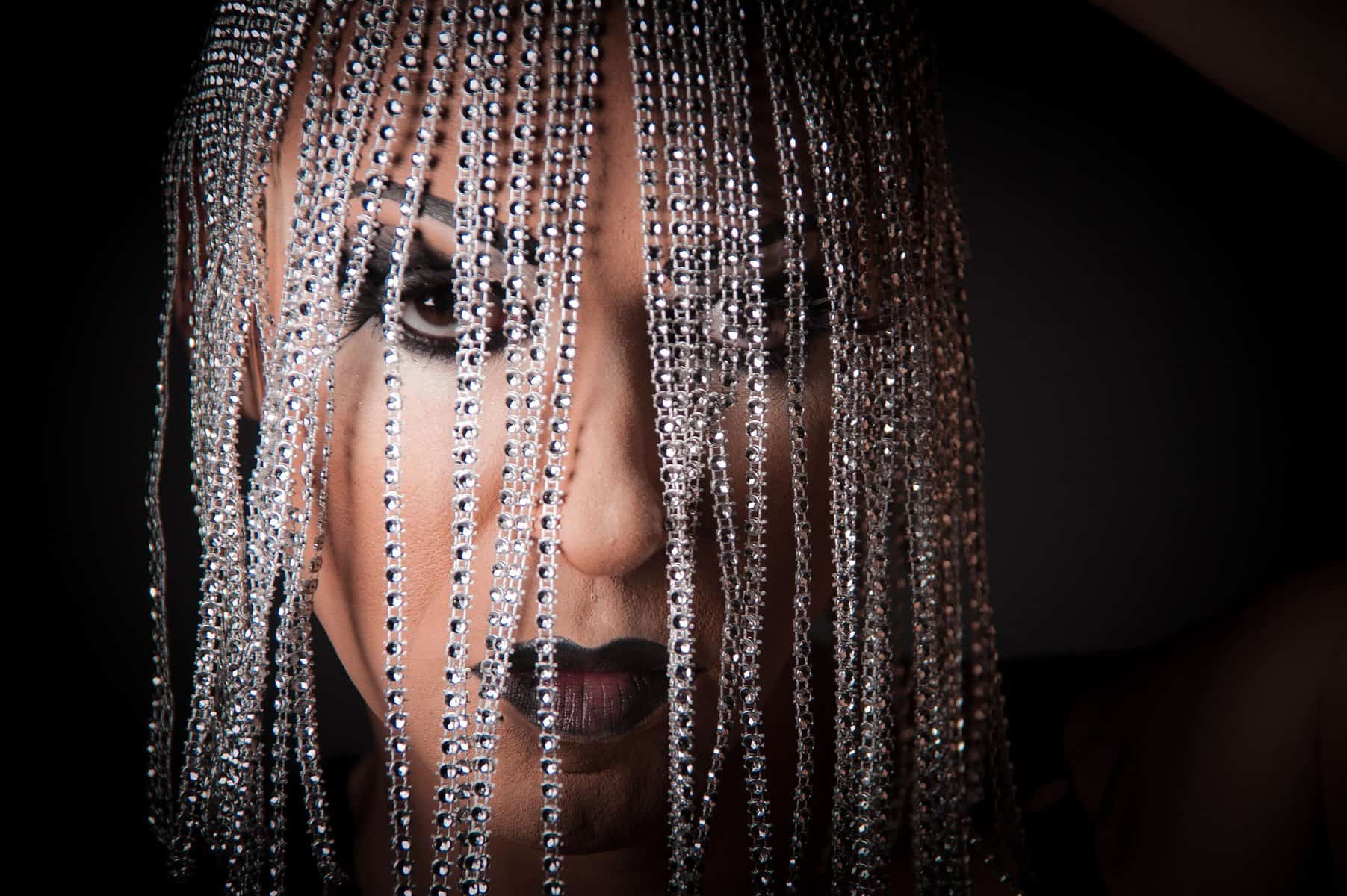 The face of a drag queen in shown close up with silver, tiny braids hanging in from of the face.