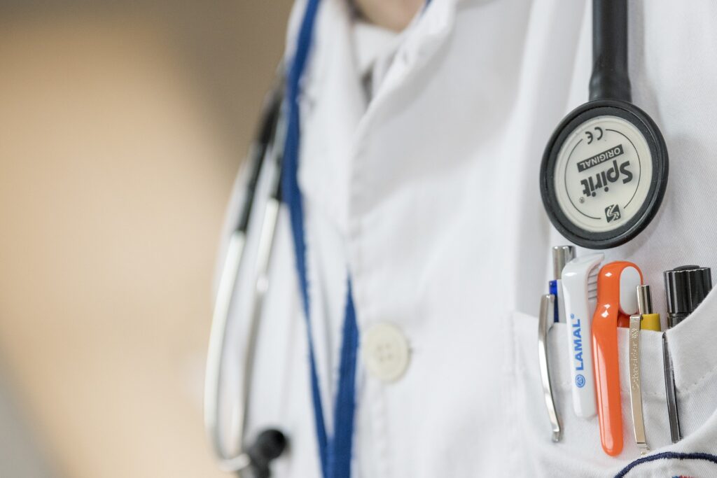 An extreme close up shows a medical person's white lab coat with pens in the pocket and a stethoscope around the neck.