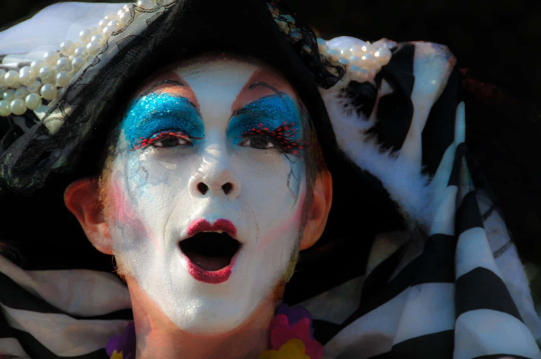 A performer with a heavily colored face like a mime is shown close up.
