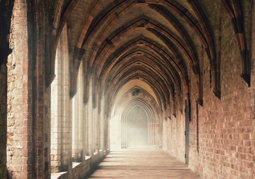 An arched stone corridor is shown at its length with soft sunlight shining in.