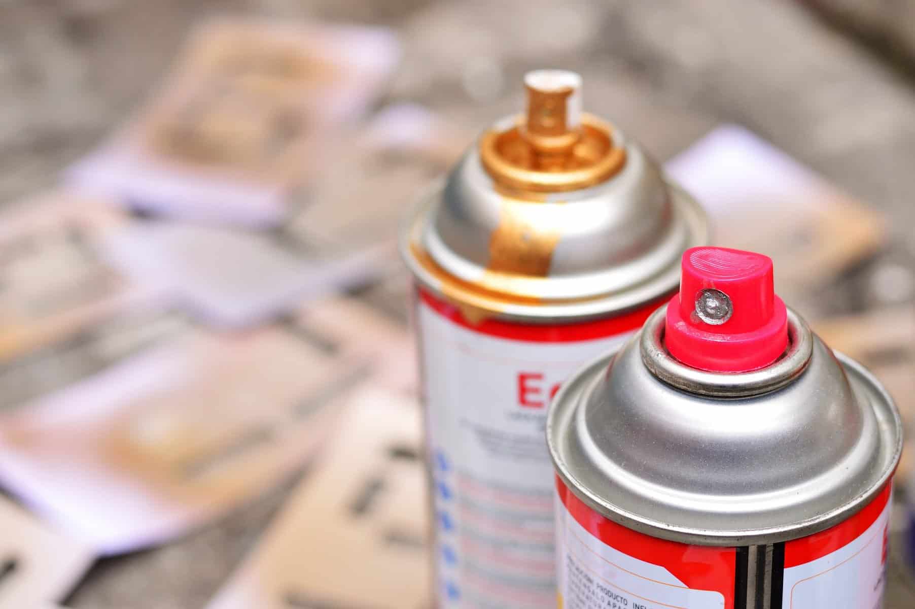 The tops of two spray paint cans are shown with blurred letter forms in the back.