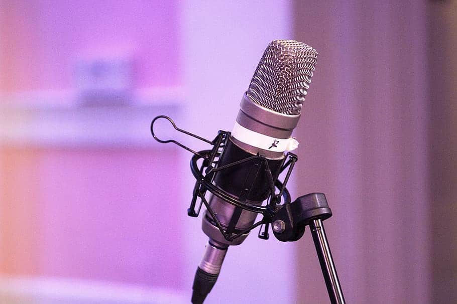A podcast microphone is shown close-up with a soft pink and purple background.