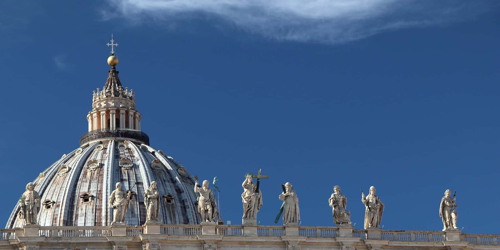 The top of the Vatican dome is seen very close up and to the left with the rooftop sculptures seen in front of it and to the right.