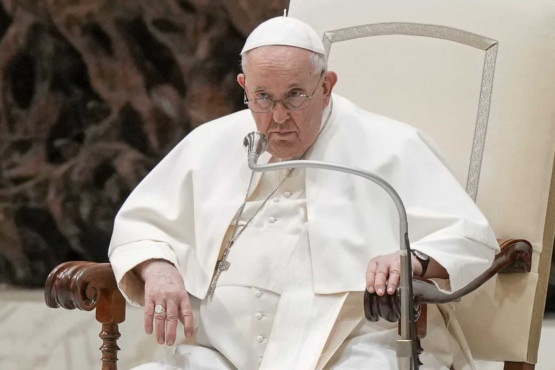 The Pope sits in a papal chair dressed in white.
