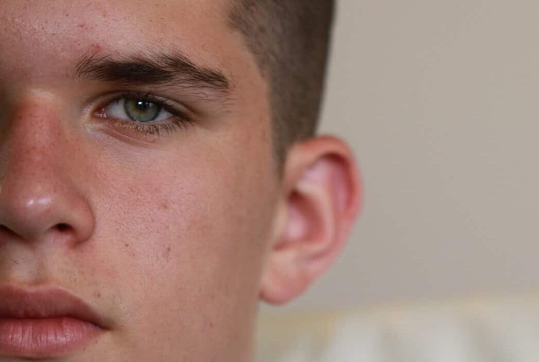 Half of a boys face is shown, from the nose over. He has unsmiling full lips, blue eyes, and a buzz cut for his dark brown hair. He is looking at the camera.