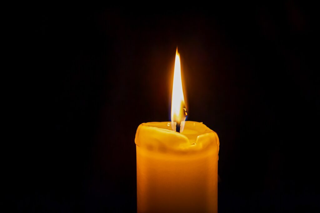 A single candle is lit against a dark background.