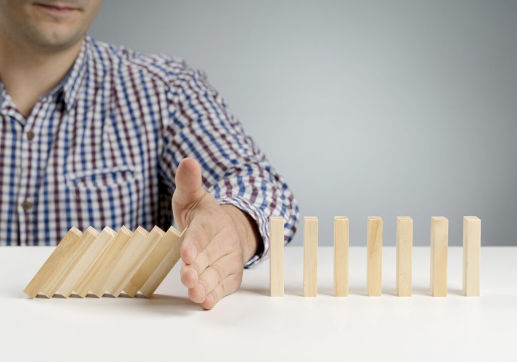 A man shown close up has his hand placed between dominos that have fallen and others that are still standing.