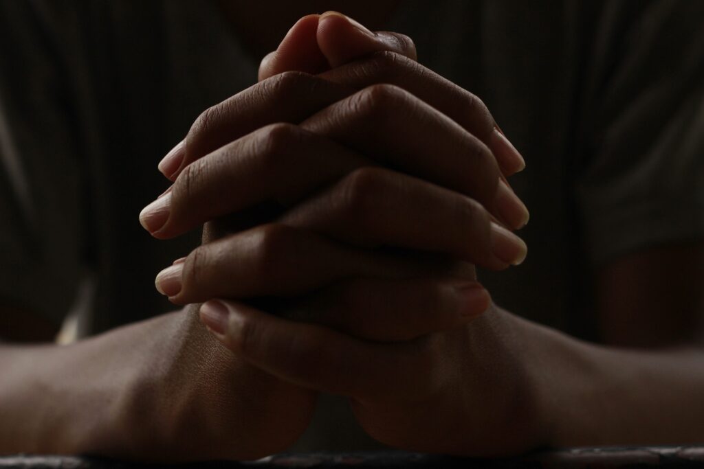 A person's hands are clasped and resting in front of them in a a very dark and moody environment.