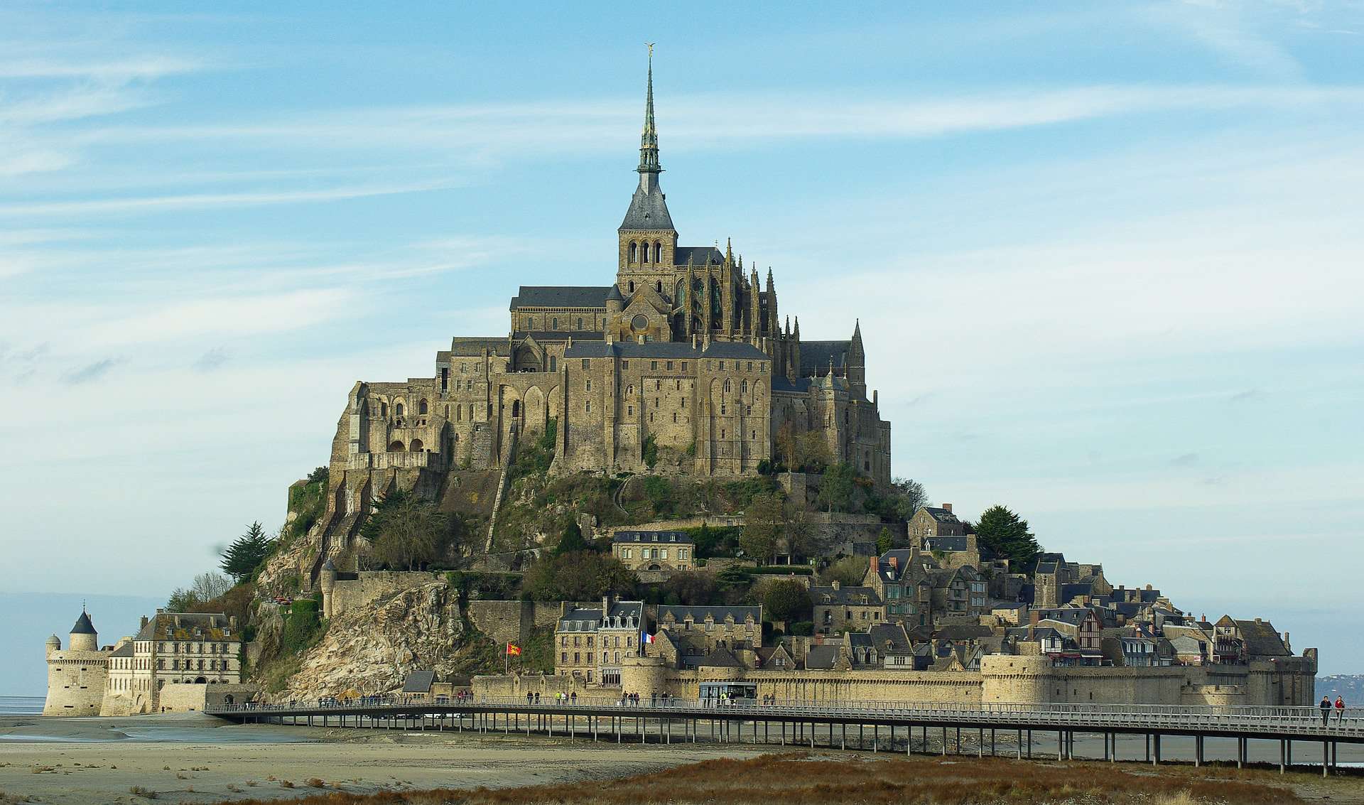 Mont Saint-Michel is shown from a distance with a blue sky and a smear of white clouds.