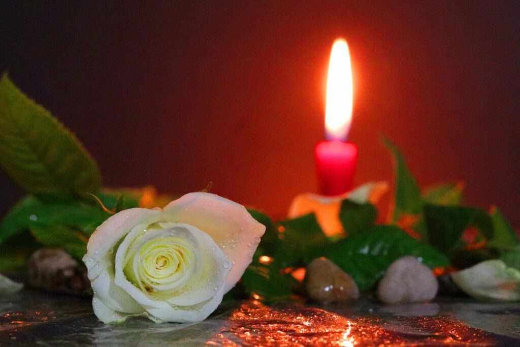A short red candle is lit with flowers resting on a table in front of it.