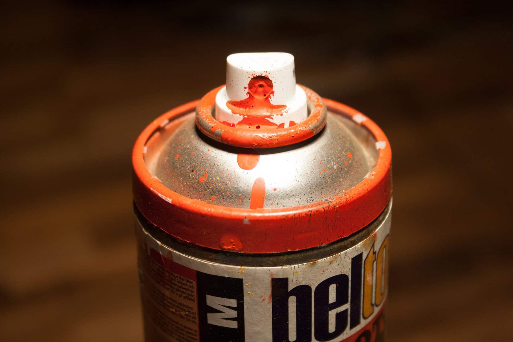 The top of a used spray-paint can is shown covered in it's orange paint.