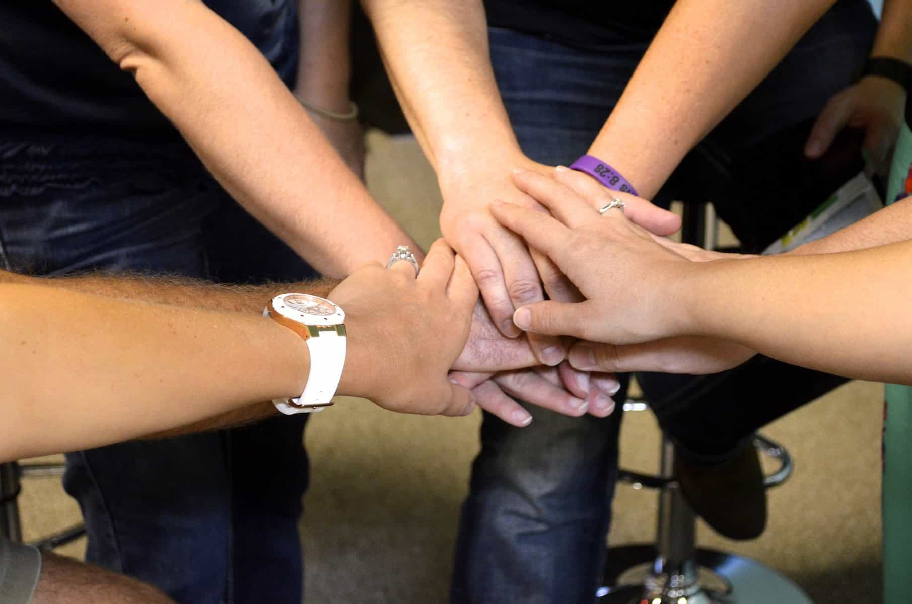The hands pf people gathered in a circle are shown stacked together.
