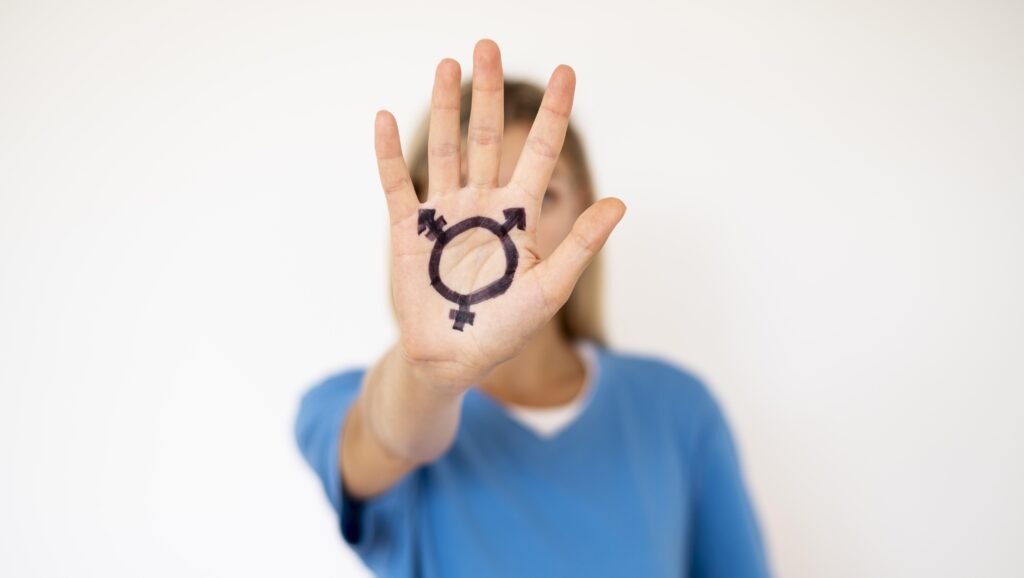 A person stands behind their forward thrust hand with the transgender sign marked on it.