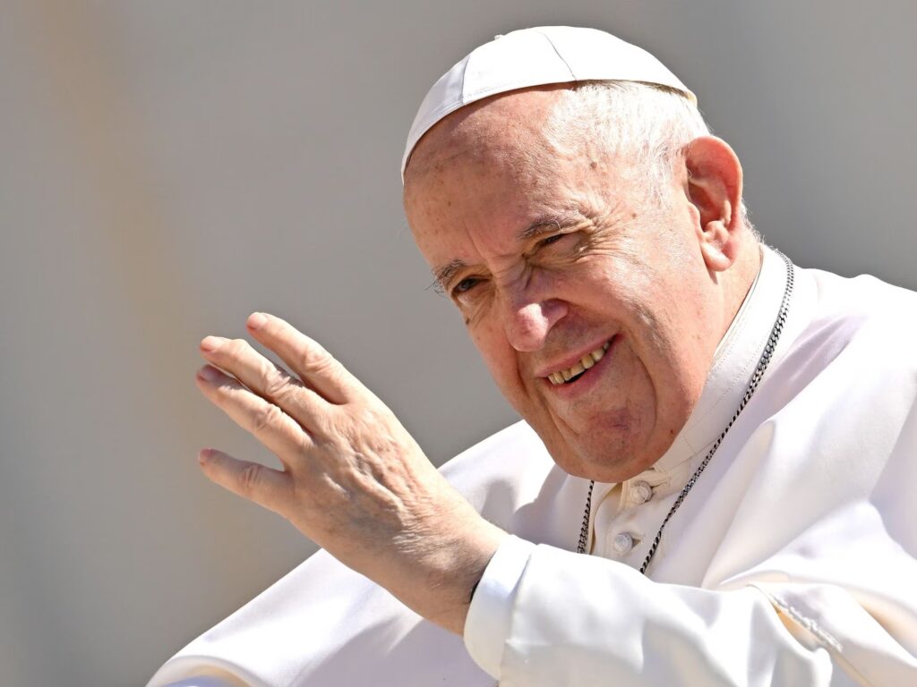 The pope is shown waving his hand and dressed in white.