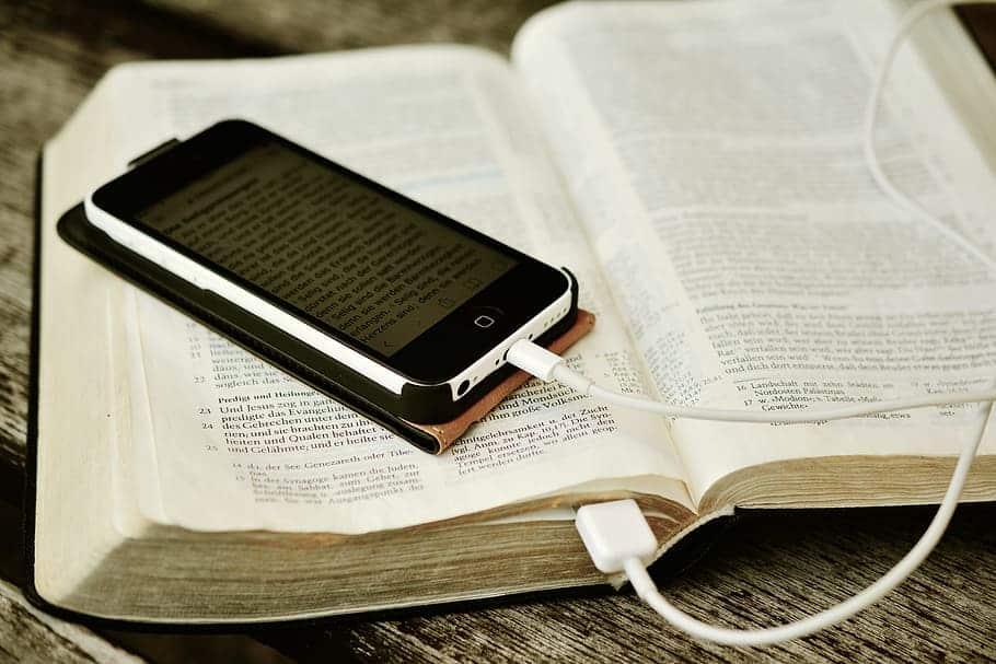 A bible is shown open faced with a mobile smart phone resting on top of it.