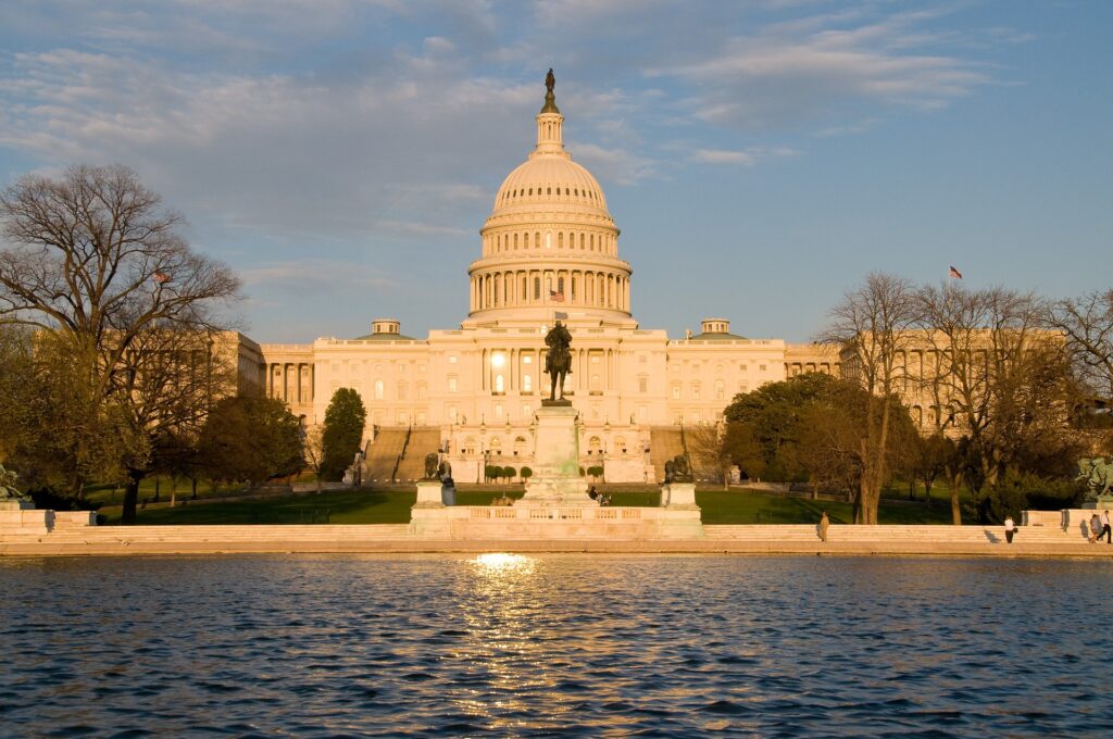 A domed capitol building is seen from across water in golden hour.