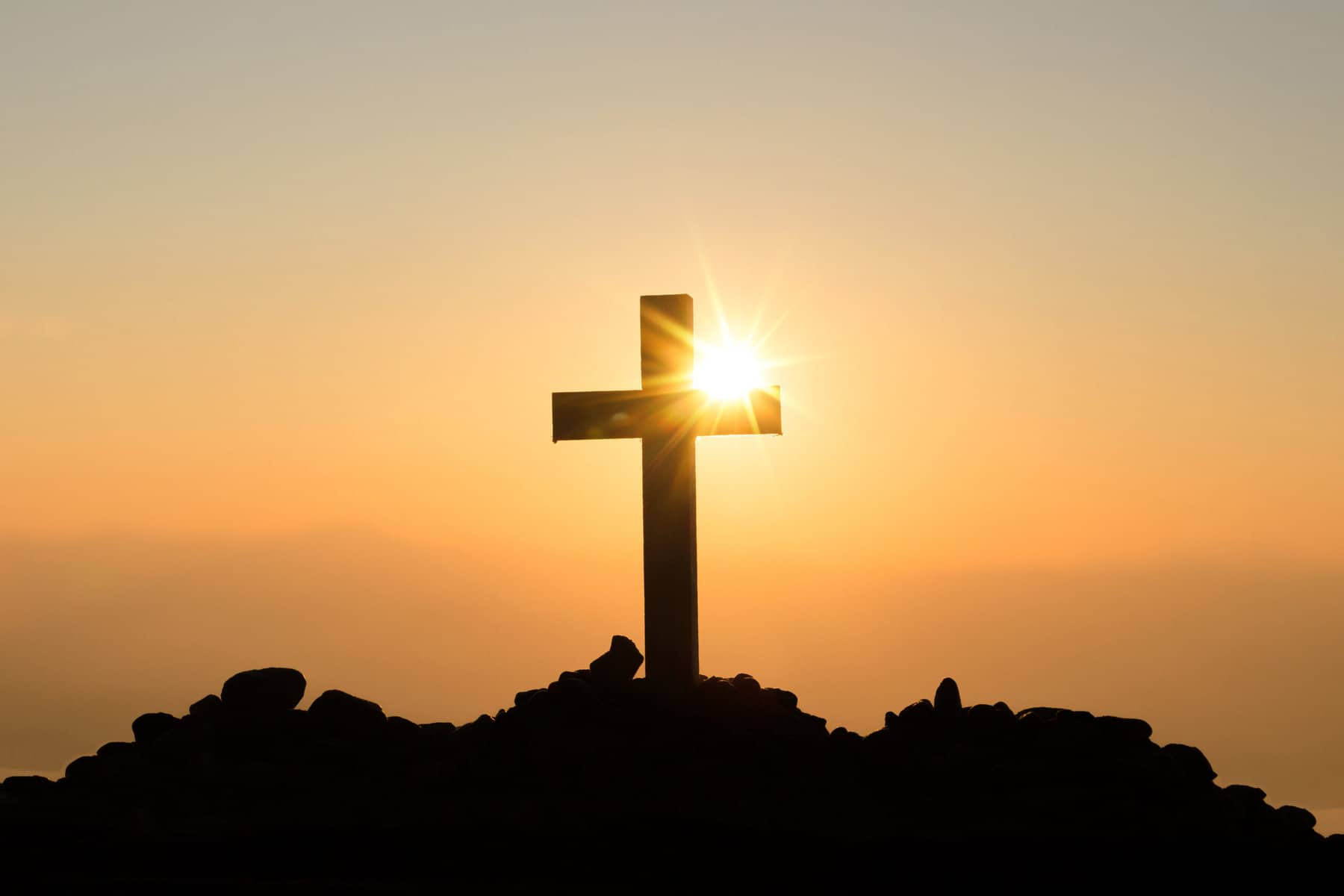 A thick beam cross is shown on a hill with the sun setting behind it.