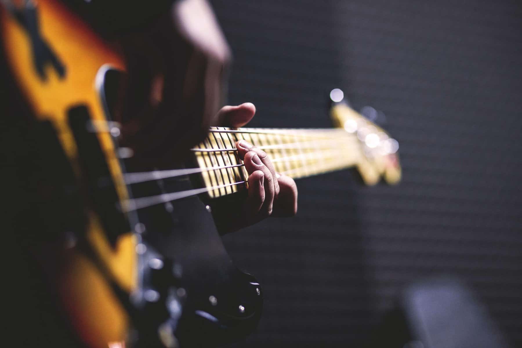 A guitar being played is seen close up from it's widest end with the players strumming hand out of focus and their fret hand in focus.