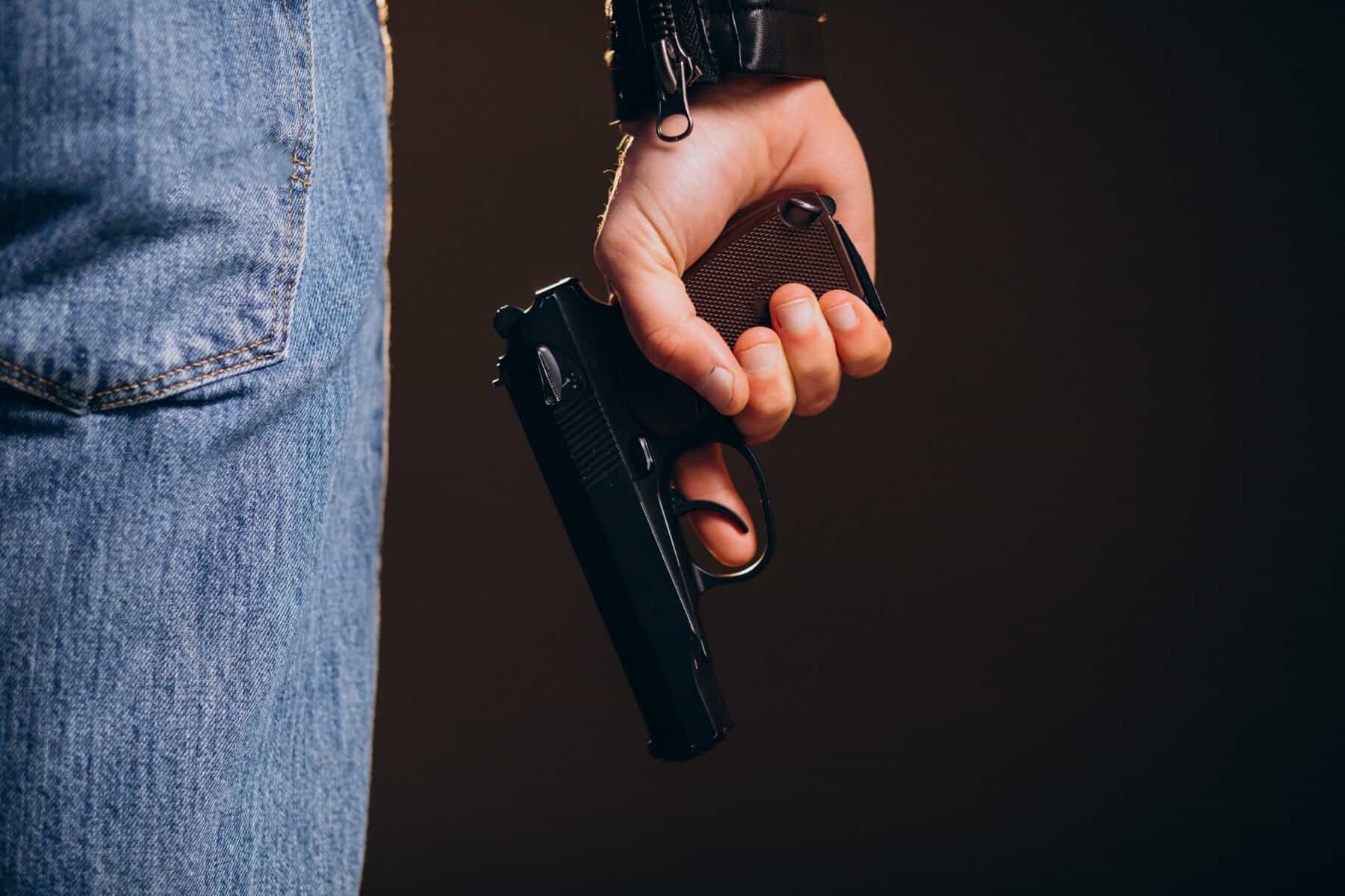 Part of a man's torso is shown from the rear with his hand at his side holding a handgun.