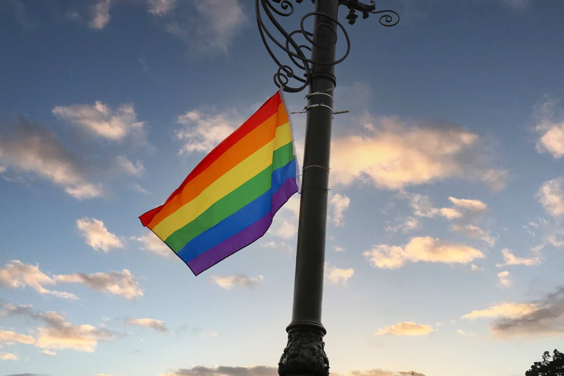 A pride flag is shown waving in the breeze atop an ornate flagpole.