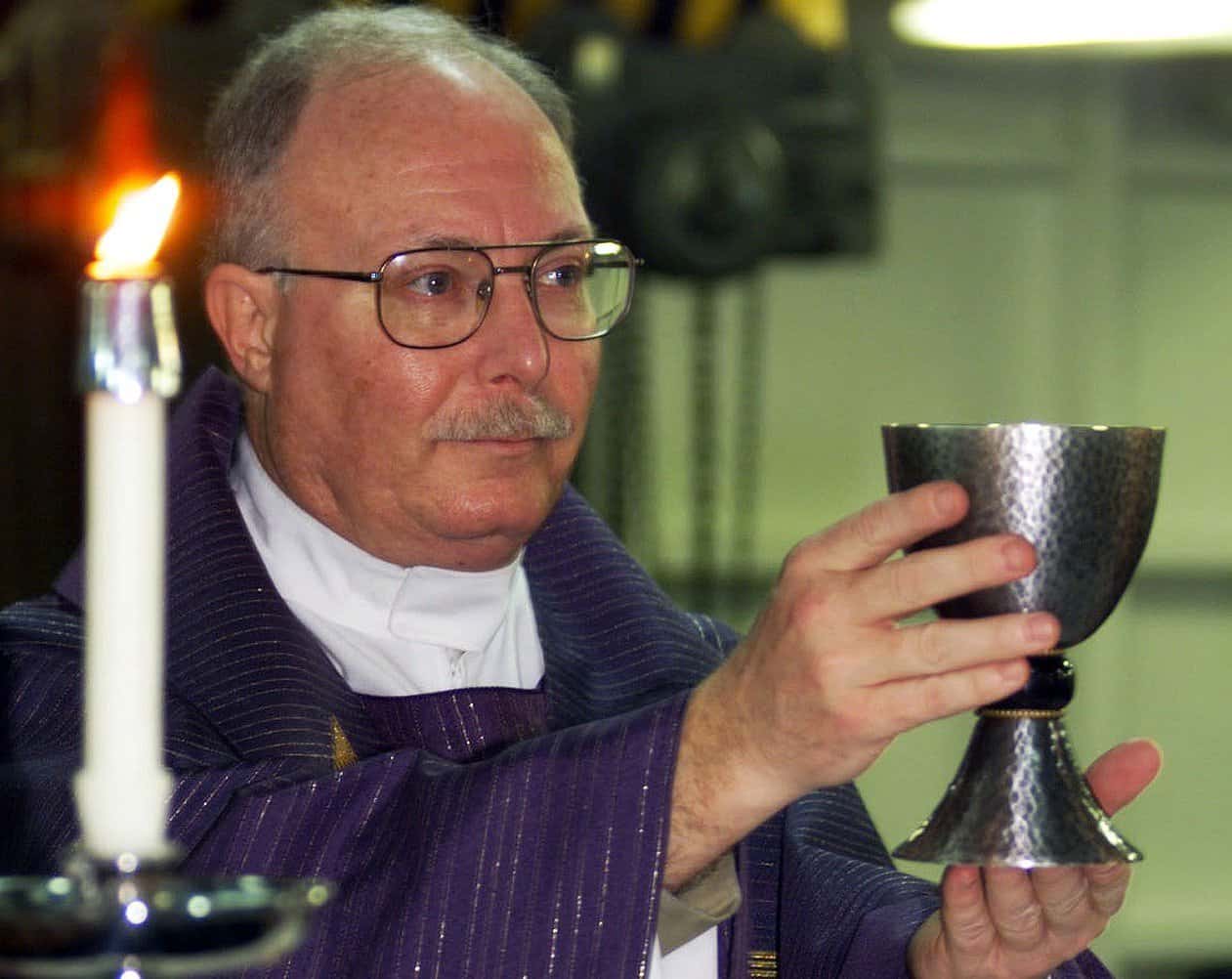 A priest holds a communion chalice aloft.