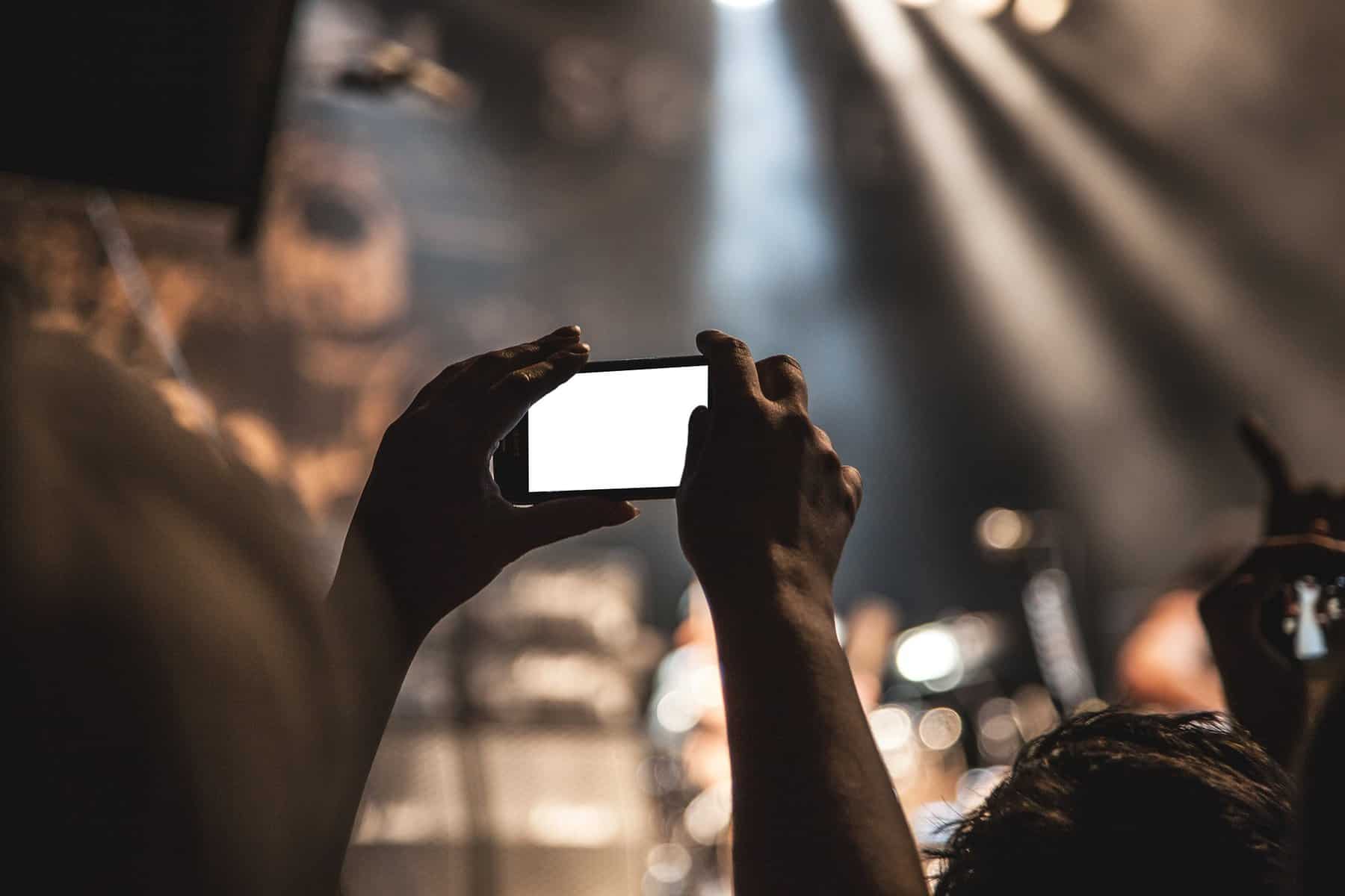 A person's hands are seen holding a cell phone recording a public event in an arena.
