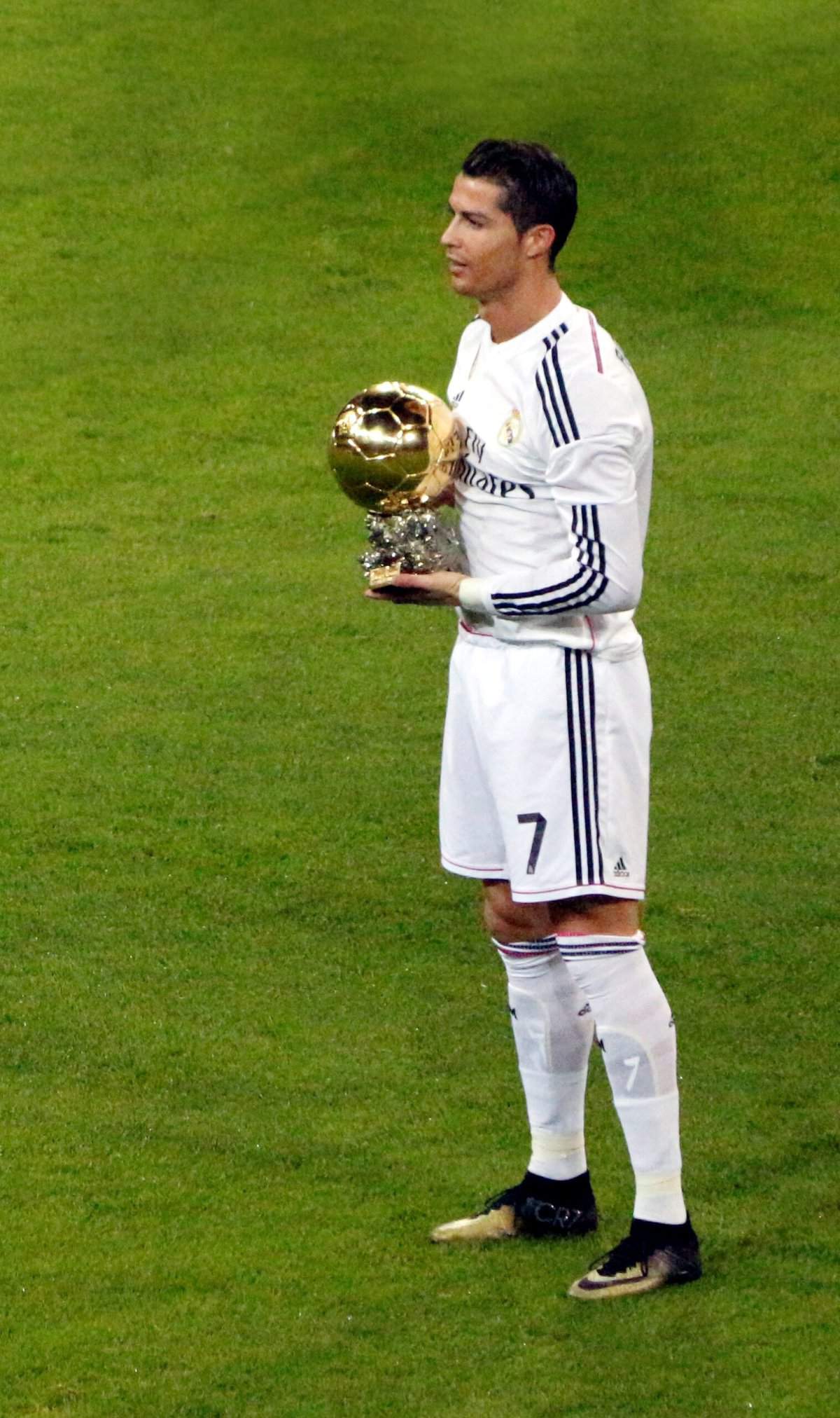 Soccer player Cristiano Ronaldo is seen on the field in a white uniform and holding a ball trophy.