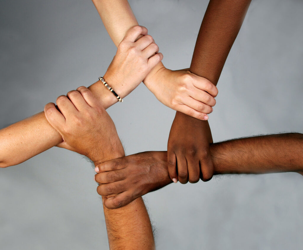 The right hands of six people of varying skin tones are shown grasping each other's wrists.