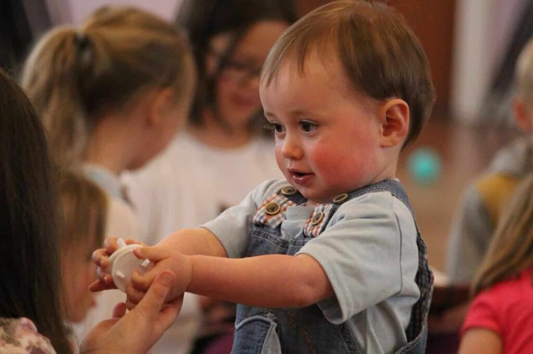 A toddler holds an item out and arms length, showing it to someone.