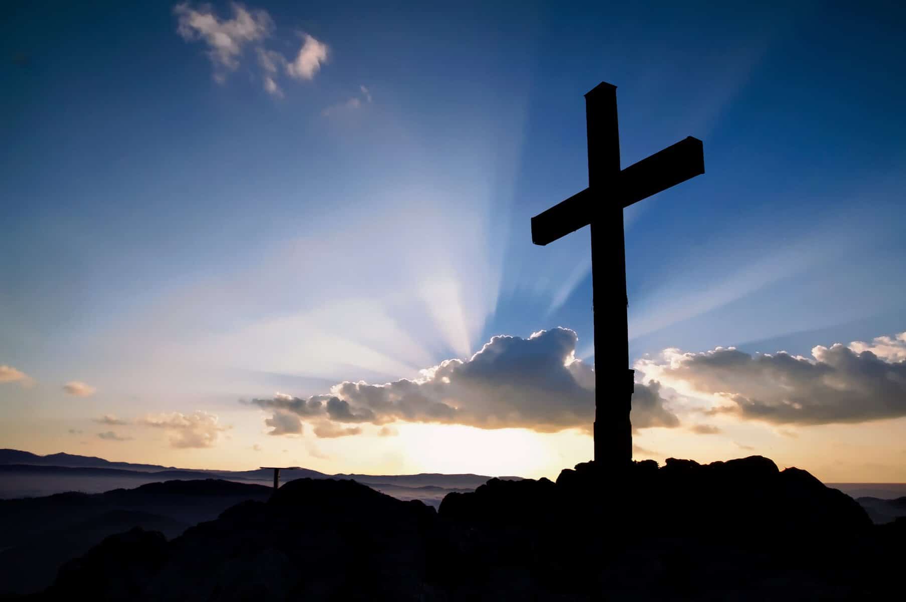 The silhouette of a cross is seen with the rising sun behind it.