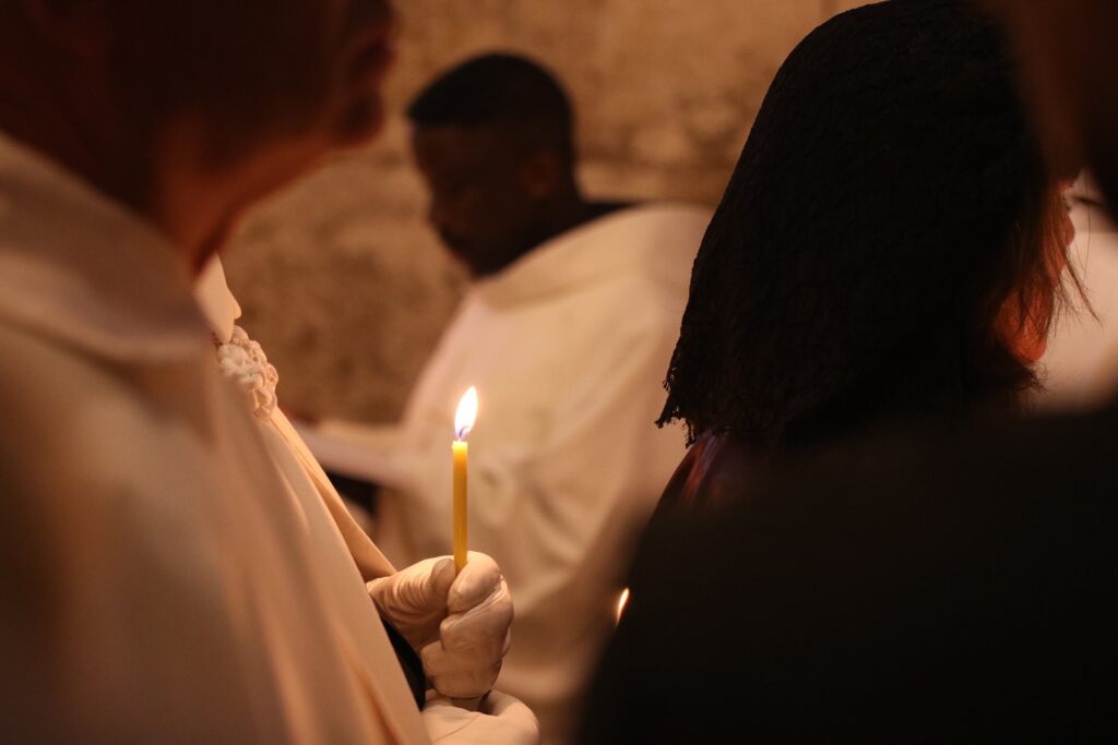 A man holds a lit candle in a white gloved hand as he stands in a line.