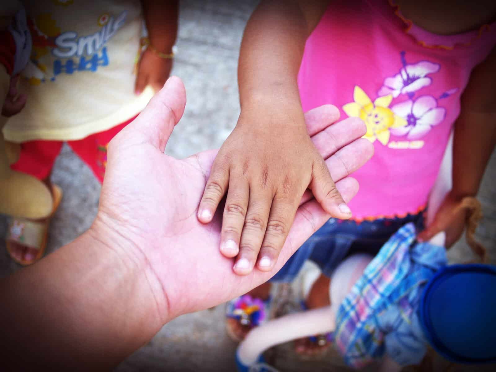 A toddler with brown skin rests their hand on the palm of a person with light skin.