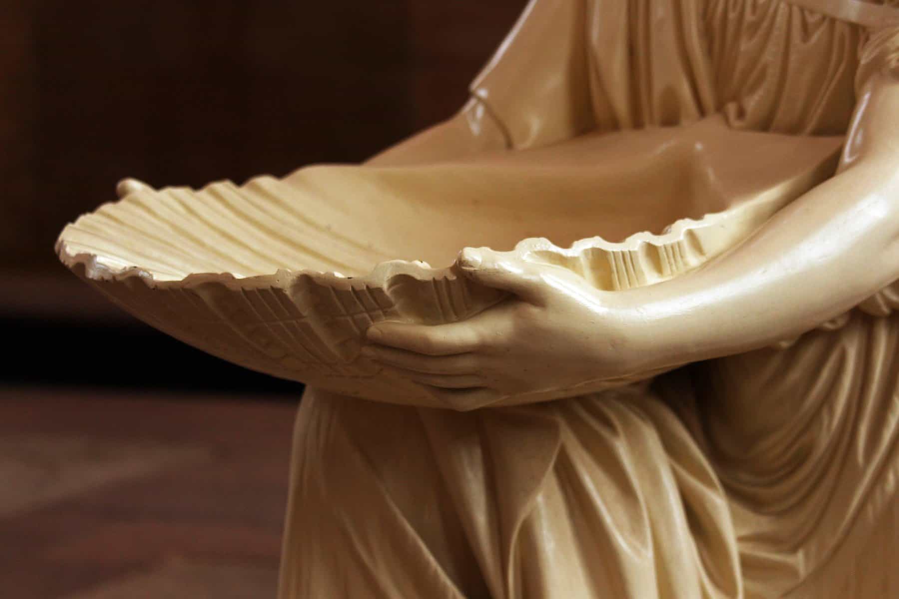 A statue's arms are shown holding a shell shaped bowl for holy water.
