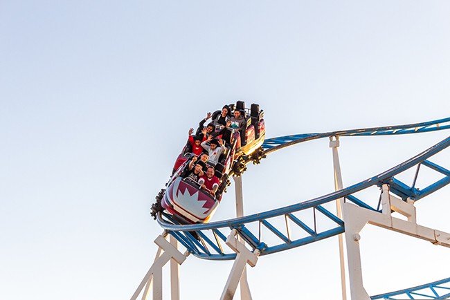 A rollercoaster is shown full of people high in the air on it's track.