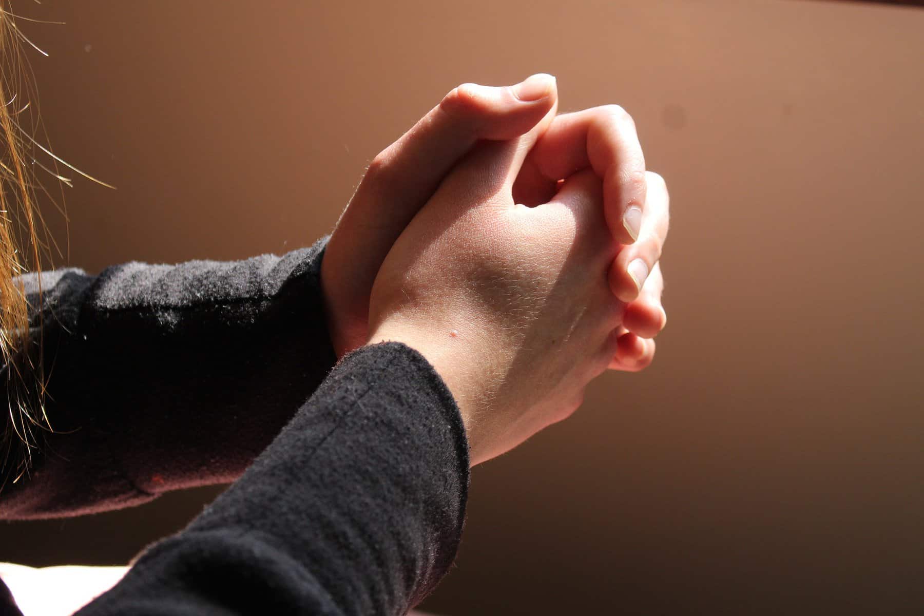 Hands are shown clasped together in front of a person in soft light.