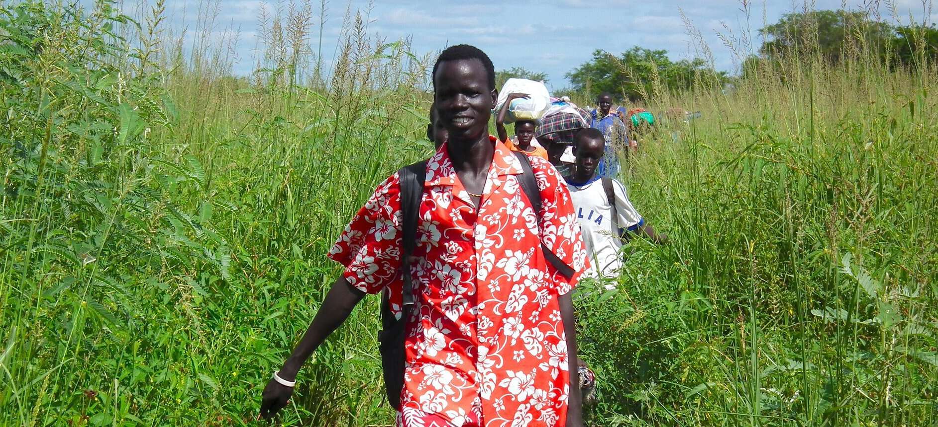 A line of Sudanese people are shown walking toward the camera.